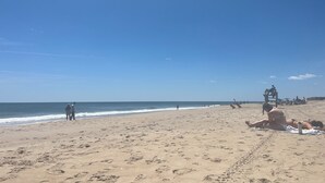 Ein Strand mit Fußspuren, einem Rettungsturm und entspannenden Menschen.