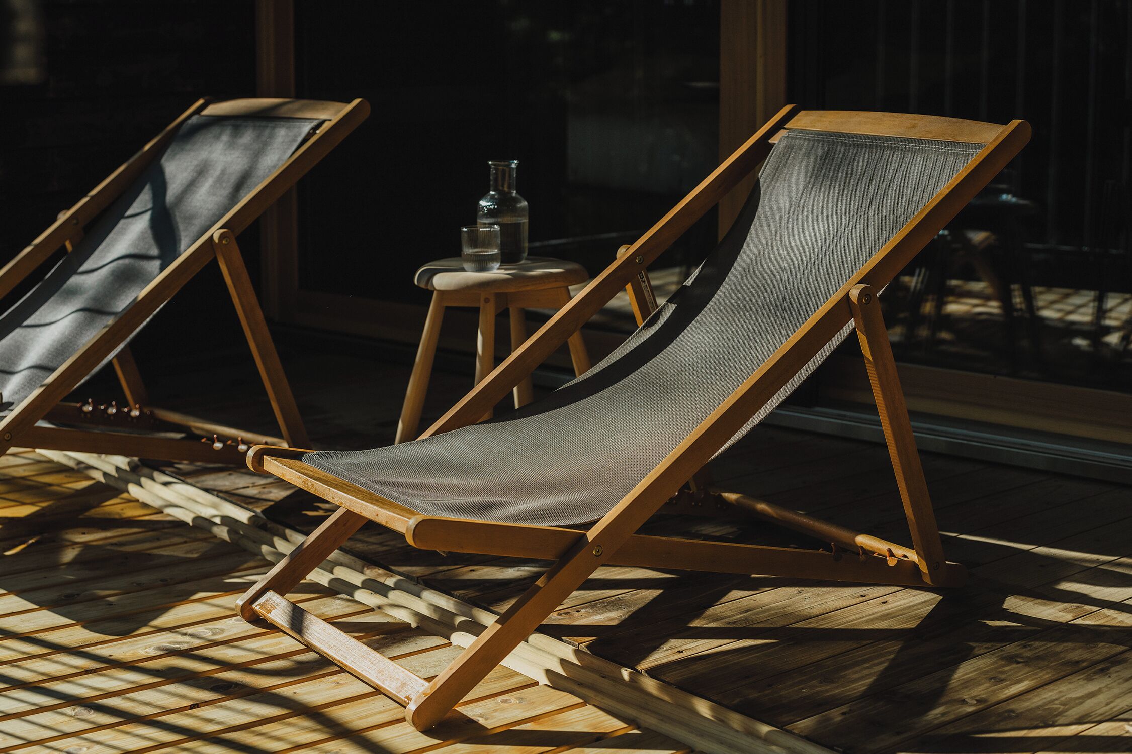 Two wooden lounge chairs with canvas seats on a wooden deck.