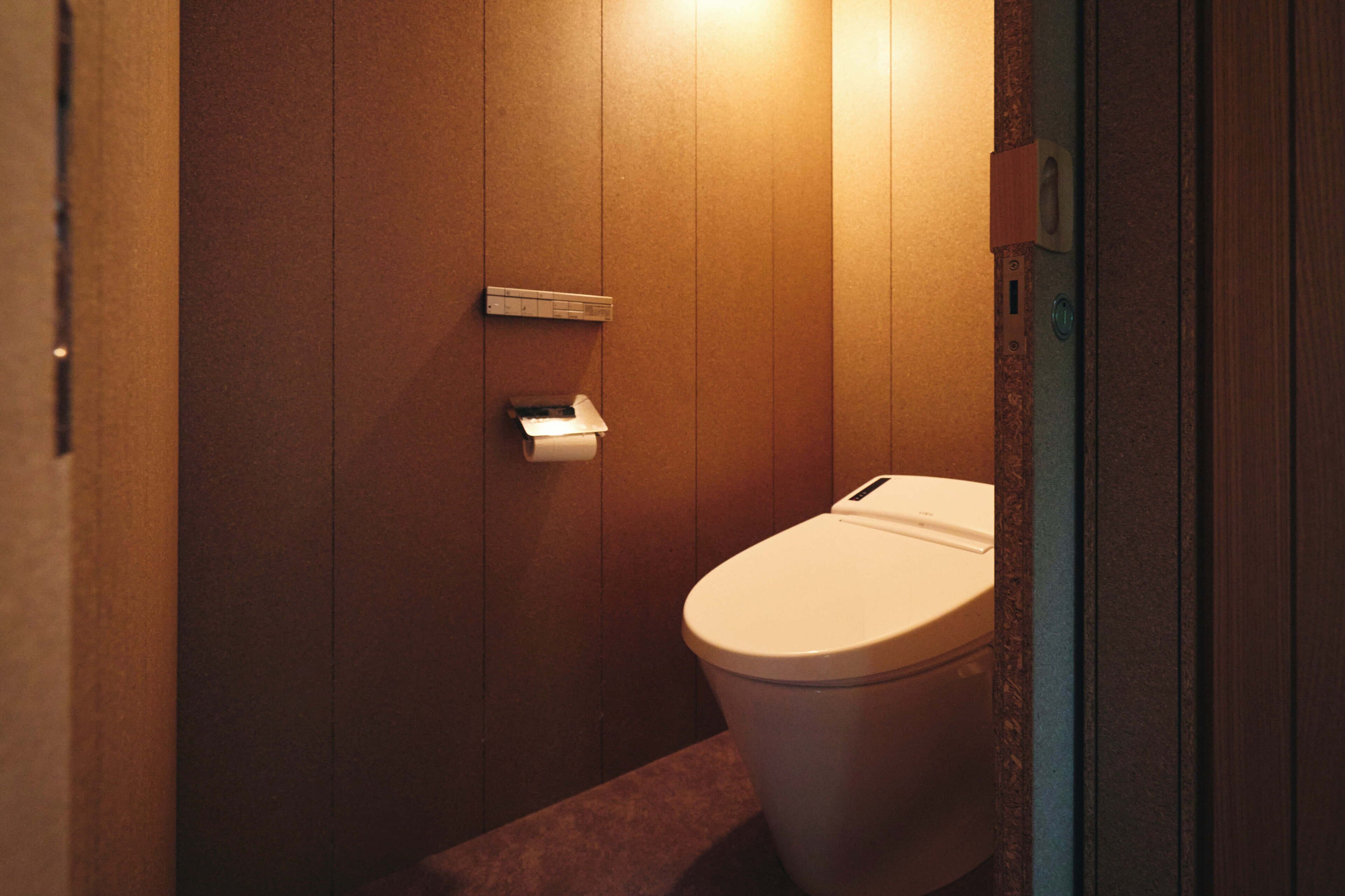 A small, private bathroom with wooden walls, a toilet, and a paper towel dispenser.