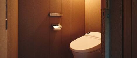 A small, private bathroom with wooden walls, a toilet, and a paper towel dispenser.