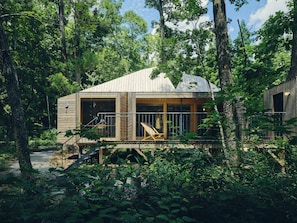 Une cabane en bois dotée de grandes fenêtres, d’une terrasse et d’un escalier menant à l’entrée.