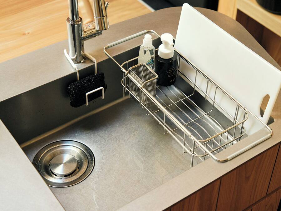 Un lavamanos de cocina con grifo de acero inoxidable, una esponja negra y un jabonero metálico con dos botellas.