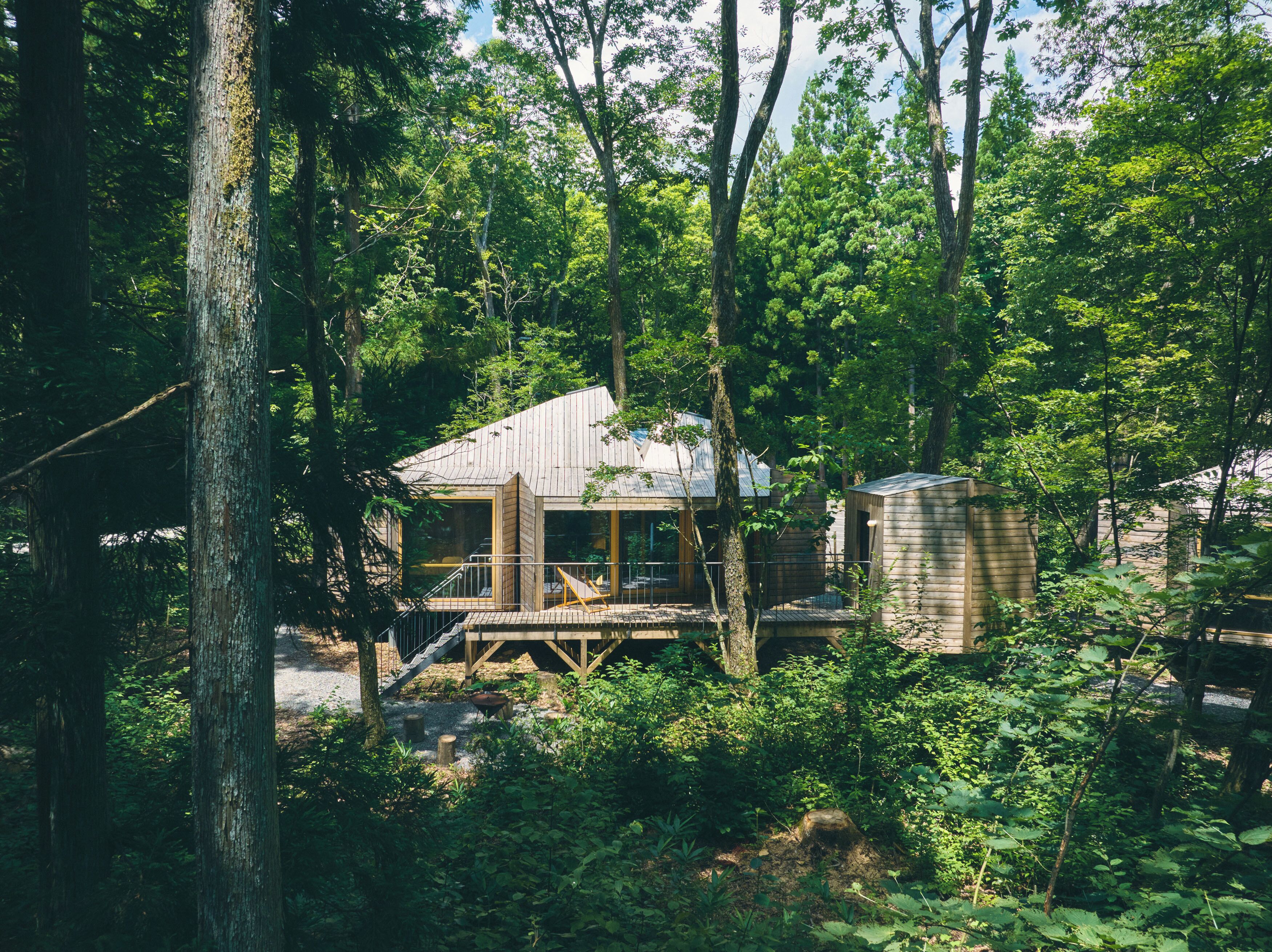 A cabin in a forest with a wooden deck and a small shed.