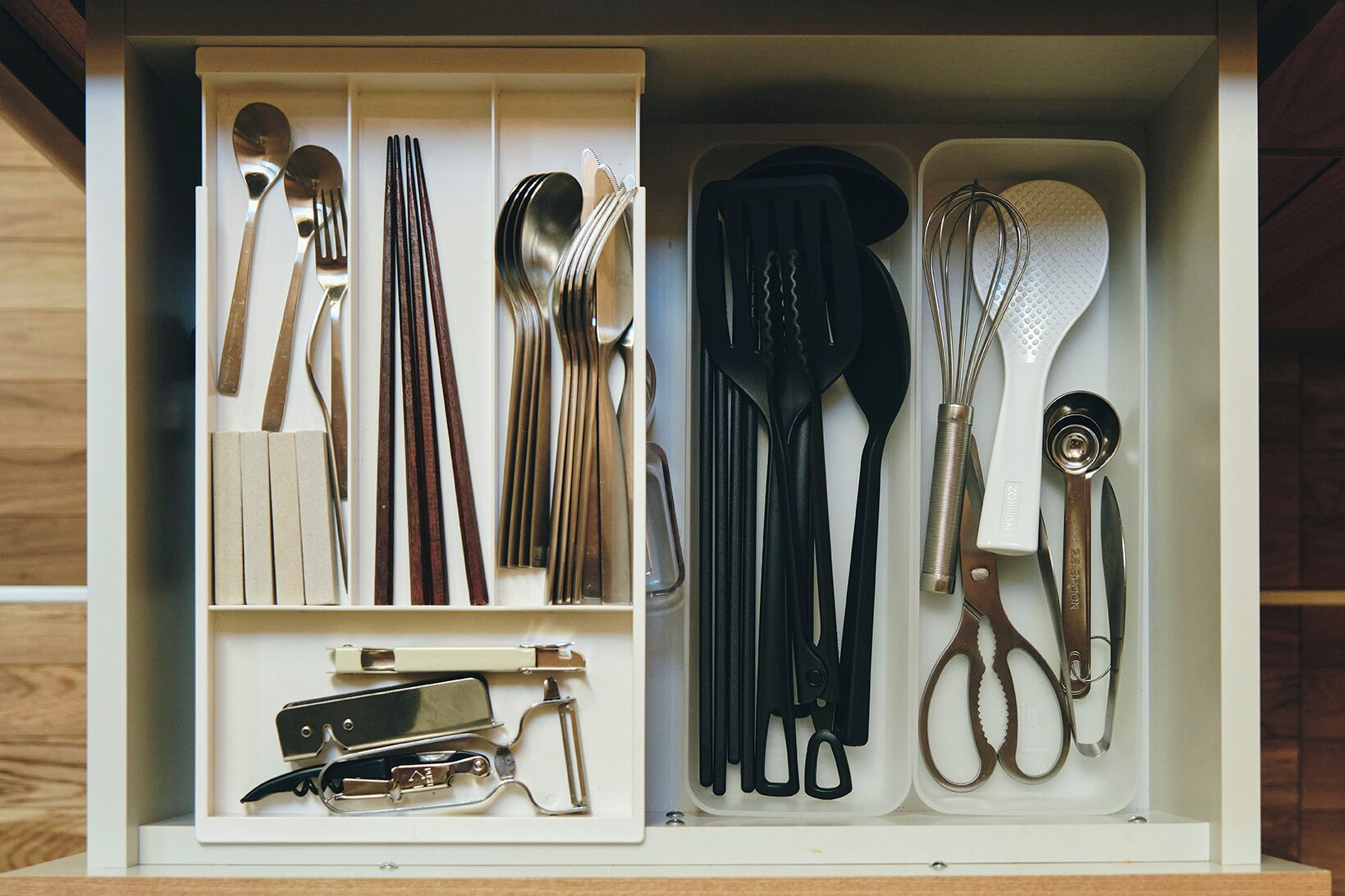Un cajón con utensilios de cocina, incluyendo cucharas, tenedores, cuchillos y un batidor.