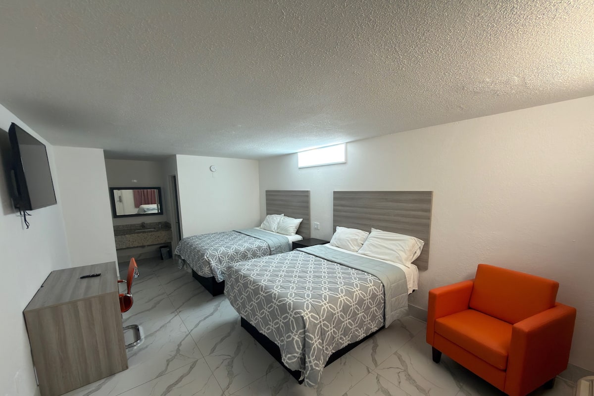 A hotel room with two beds, a TV, a bathroom, and an orange chair.
