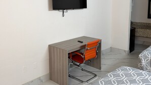 Ett hotellrum med en platt-TV som är monterad på väggen, ett skrivbord i trä med en röd stol och en säng med ett mönstrat överdrag.