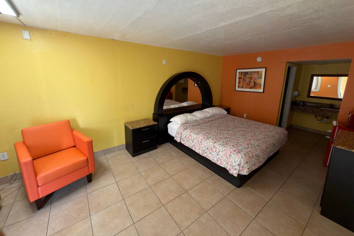 A bedroom with a bed, a nightstand, a chair, and a bathroom visible through an open door.