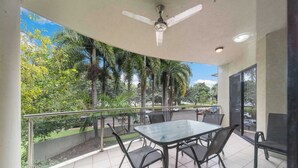 Ein Balkon mit Tisch und Stühlen, einem Deckenventilator und Blick auf Palmen und eine Straße.