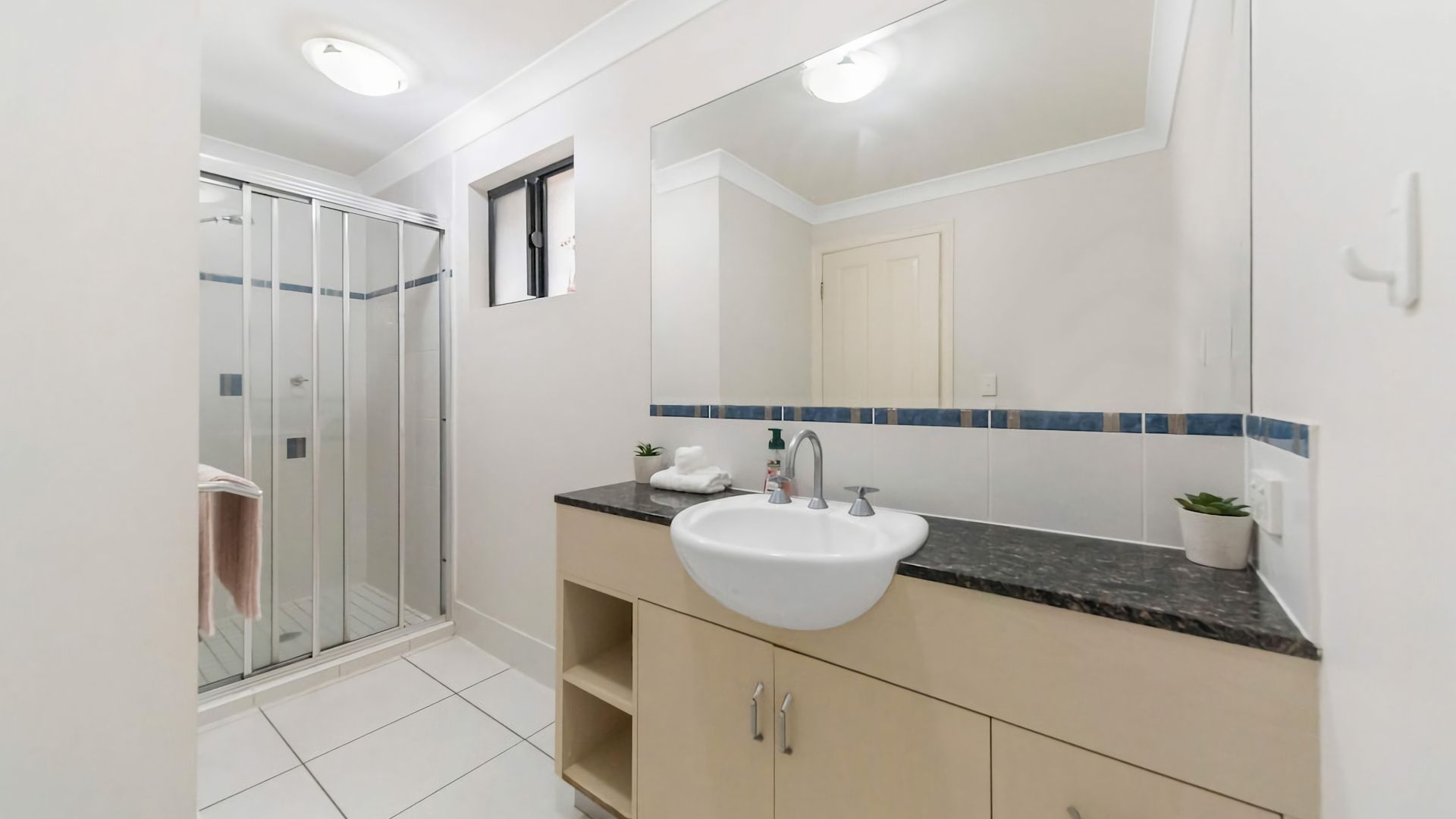 A bathroom with a glass shower enclosure, a white sink, and a mirror with a blue-tiled backsplash.