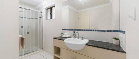 A bathroom with a glass shower enclosure, a white sink, and a mirror with a blue-tiled backsplash.