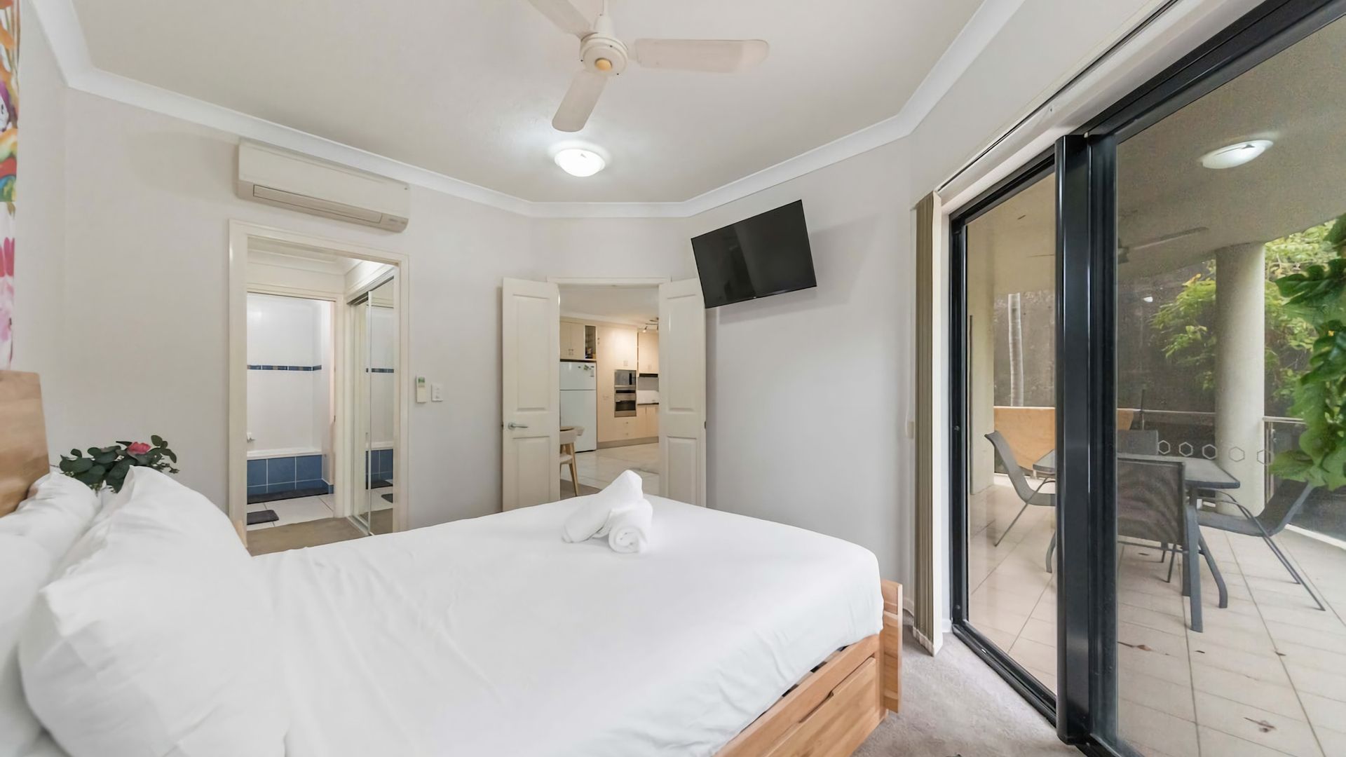 A bedroom with a bed, a ceiling fan, and a sliding glass door leading to a balcony.