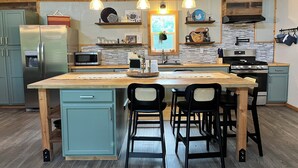 Une cuisine moderne dotée d’un îlot central, de meubles en bois, d’appareils électroménagers en acier inoxydable et de luminaires suspendus.
