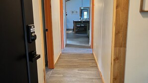 Un couloir doté d’un plancher en bois, une porte équipée d’un clavier pour l’ouverture à code, et une vue sur une pièce contenant un bureau et une chaise.