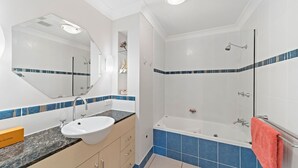 A bathroom with a sink, mirror, vanity, and a bathtub.