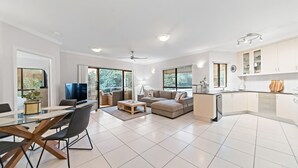 A modern living space with a dining area, a sofa set, a kitchen, and large windows.