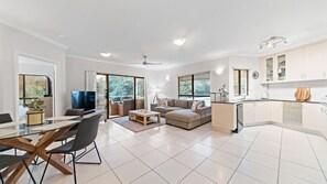A modern living space with a dining area, a sofa set, a kitchen, and large windows.