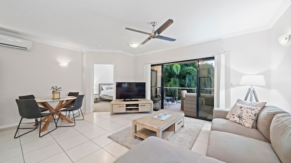 A modern living room with a flat-screen TV, a ceiling fan, a dining area with chairs, and a sofa.