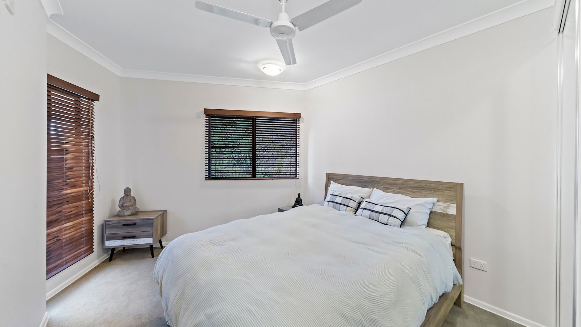 A bedroom with a bed, a nightstand, a ceiling fan, and a window with blinds.