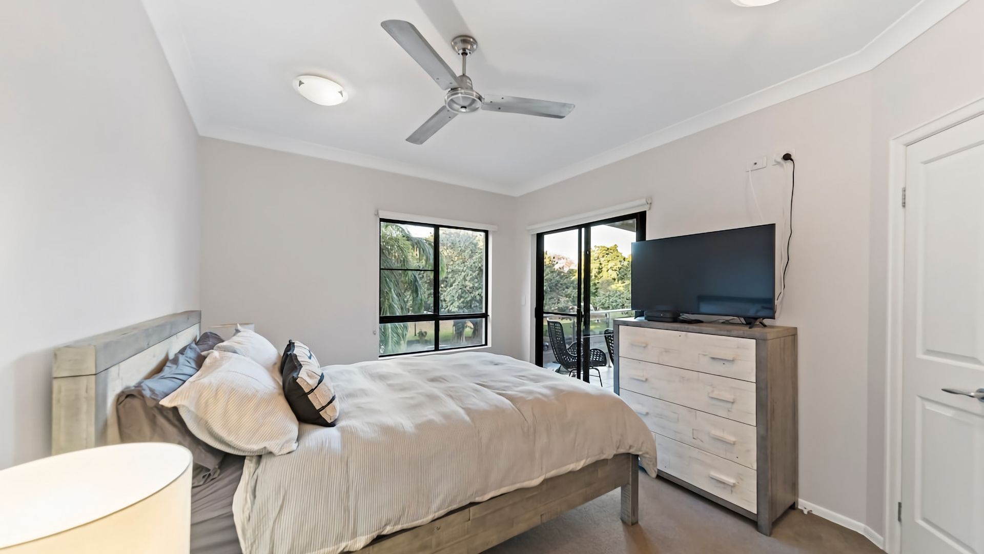 Ein Schlafzimmer mit Bett, Fernseher, Deckenventilator und Blick ins Freie durch ein Fenster.