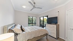 A bedroom with a bed, a television, a ceiling fan, and a view of the outdoors through a window. - Beachside 2 bed 2 bath unit (North Ward)