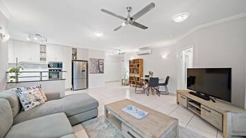 A modern living room with a sofa, coffee table, TV, and a dining area with chairs and a table.