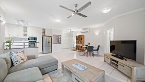 A modern living room with a sofa, coffee table, TV, and a dining area with chairs and a table. - Beachside 2 bed 2 bath unit (North Ward)