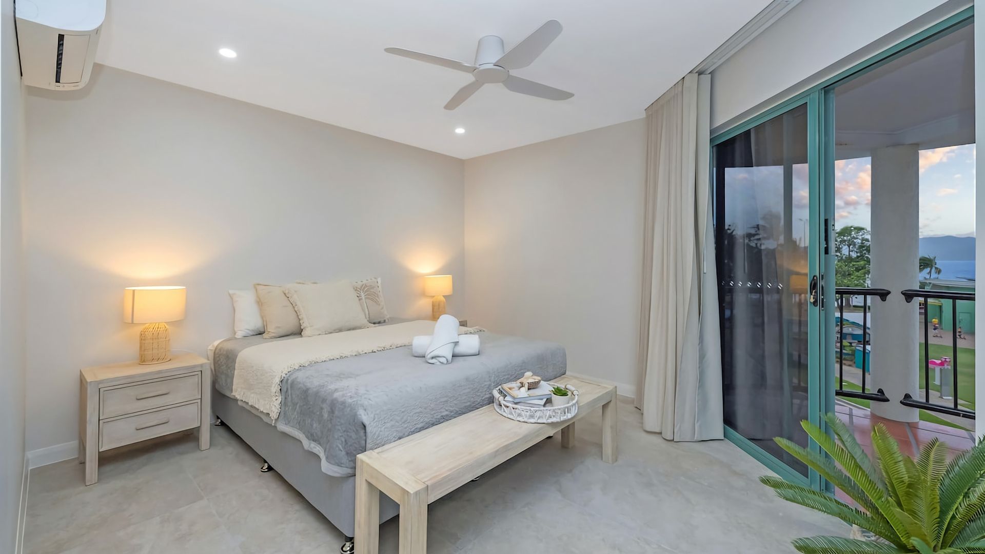 A bedroom with a bed, bedside lamps, a ceiling fan, and a balcony with a view.