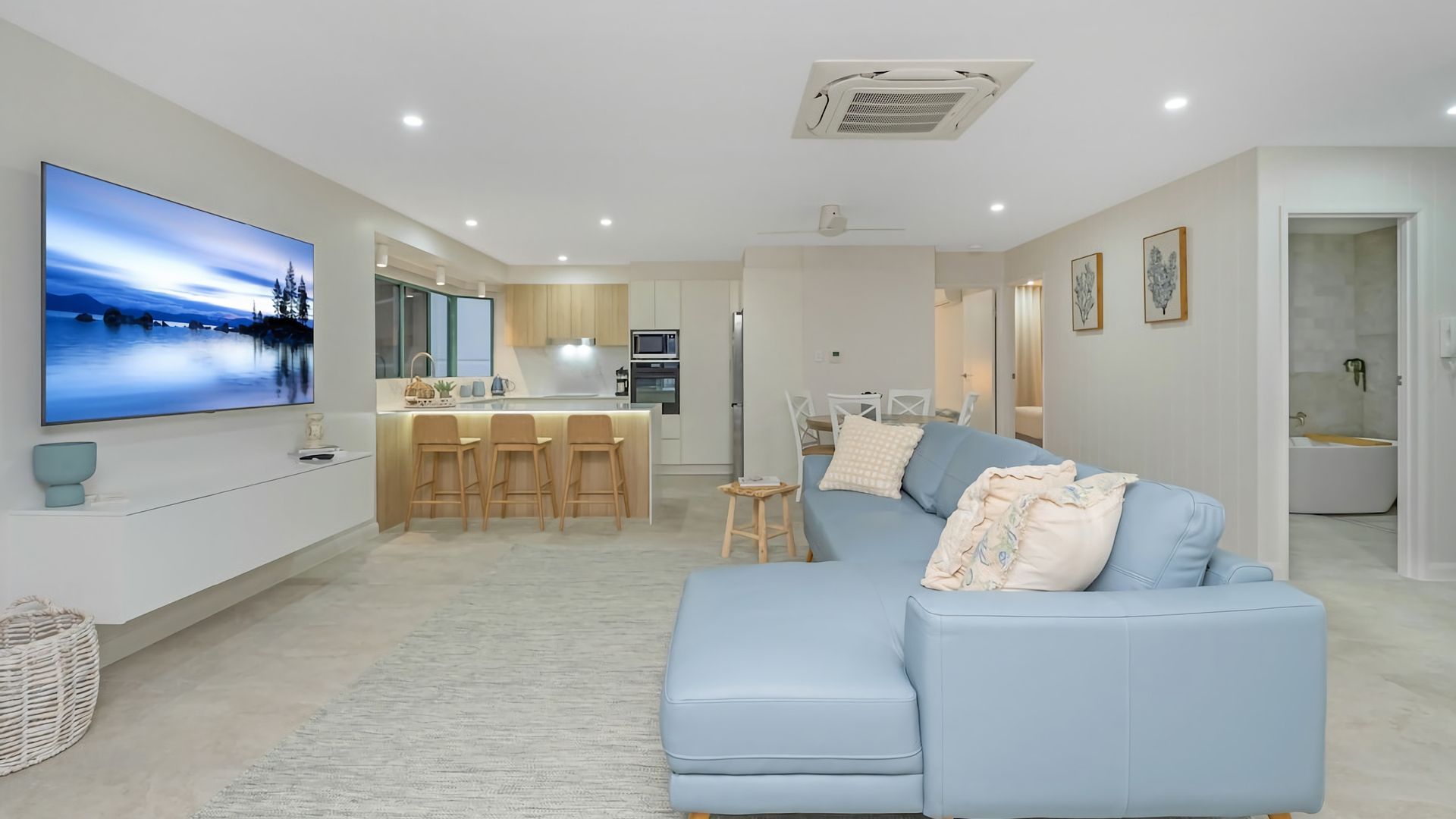 A modern living room with a blue sofa, a flat-screen TV, and a kitchen in the background.