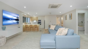 A modern living room with a blue sofa, a flat-screen TV, and a kitchen in the background.