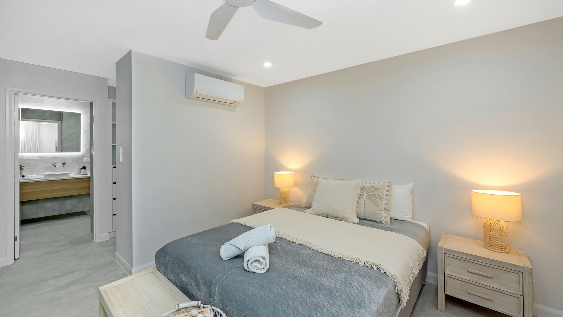 A bedroom with a bed, bedside lamps, a ceiling fan, and an air conditioning unit.