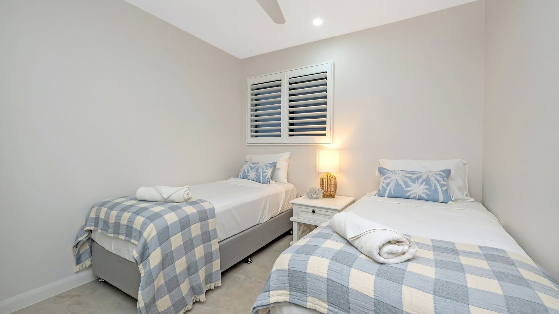 A bedroom with two beds, a nightstand, a lamp, and a ceiling fan.