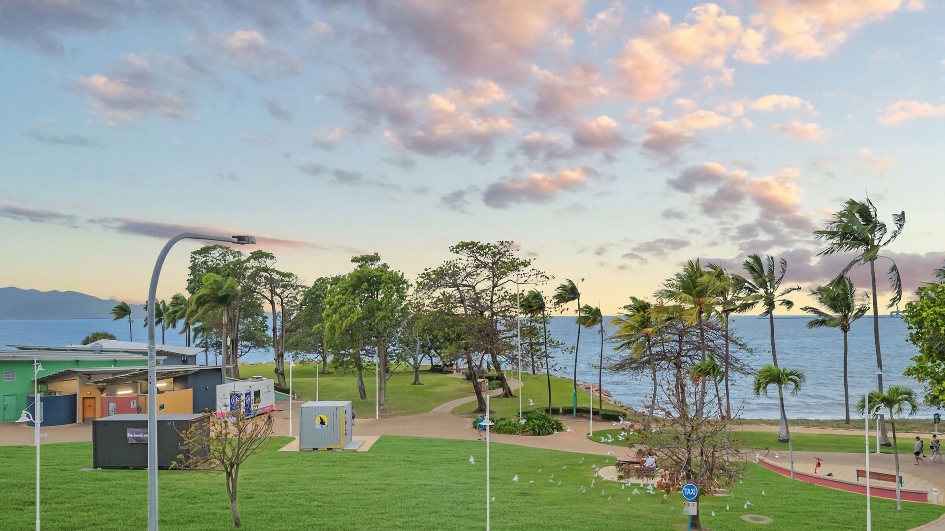 A coastal park with a pathway, trees, and a view of the sea.
