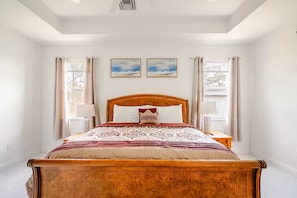 Un dormitorio con una cama de madera, dos cuadros en la pared y un ventanal con cortinas.