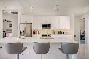 Una cocina moderna con armarios blancos, un refrigerador de acero inoxidable, un microondas y una isla grande con taburetes de bar.