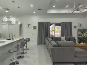 Un espacio moderno para vivir con área de cocina, zona de estar con sofá y sillones, y ventilador de techo.