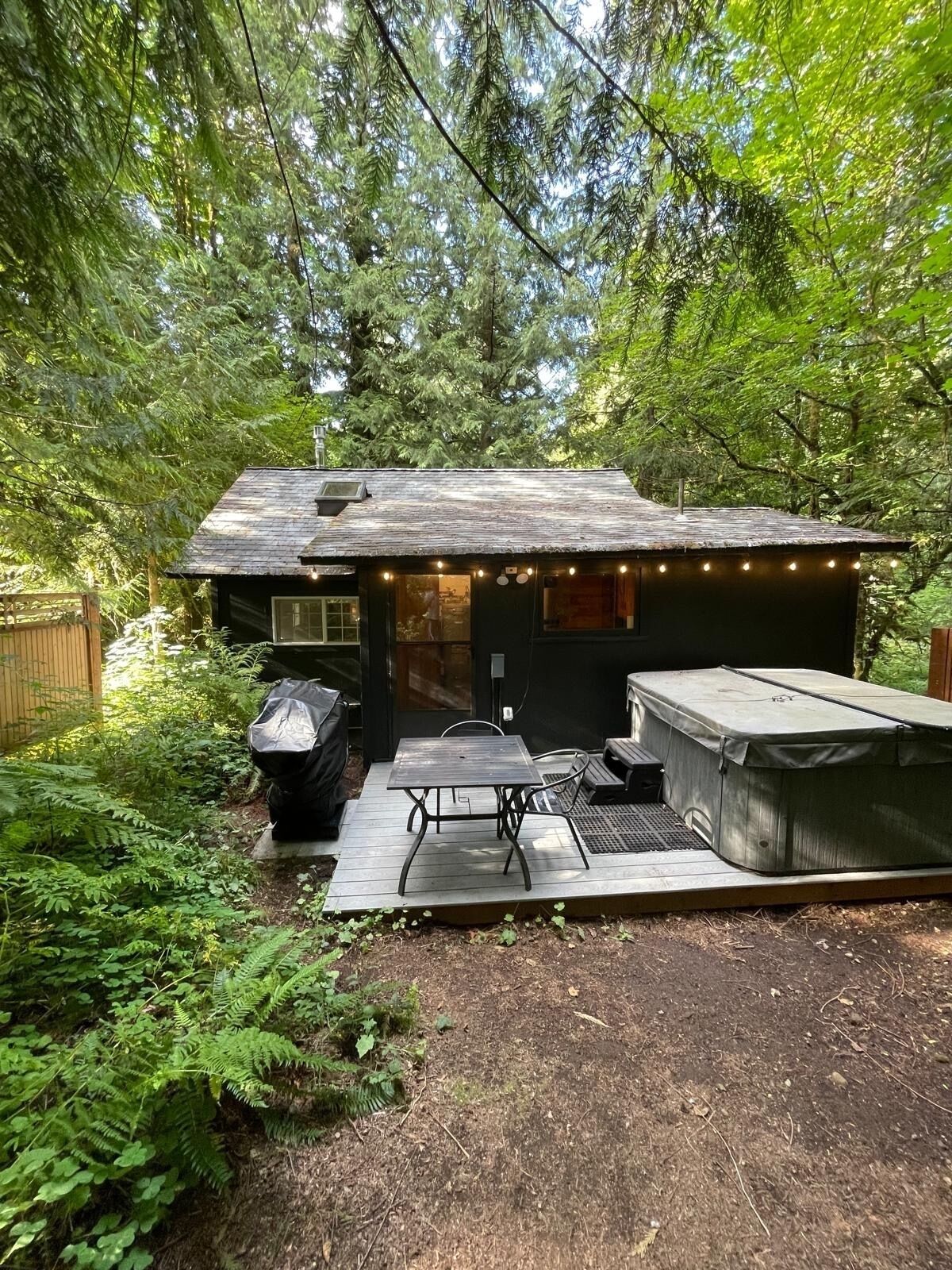 A small cabin with a deck, outdoor seating, and a hot tub.