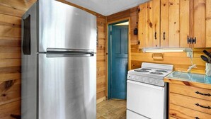 Une cuisine de taille réduite avec des murs en bois, un réfrigérateur en acier inoxydable, une cuisinière blanche et des armoires en bois.