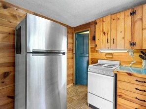 Eine kleine Küche mit Holzwänden, einem Edelstahlkühlschrank, einem weißen Herd und Holzschränken.