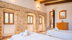 A room with stone walls, two beds with white linens, a wooden dresser, and a mirror.