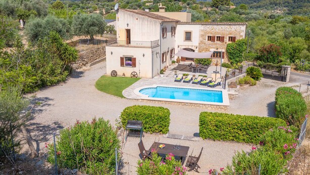 A two-story house with a swimming pool, surrounded by greenery and hills.