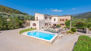 A villa with a swimming pool, outdoor seating, and a view of the surrounding hills.
