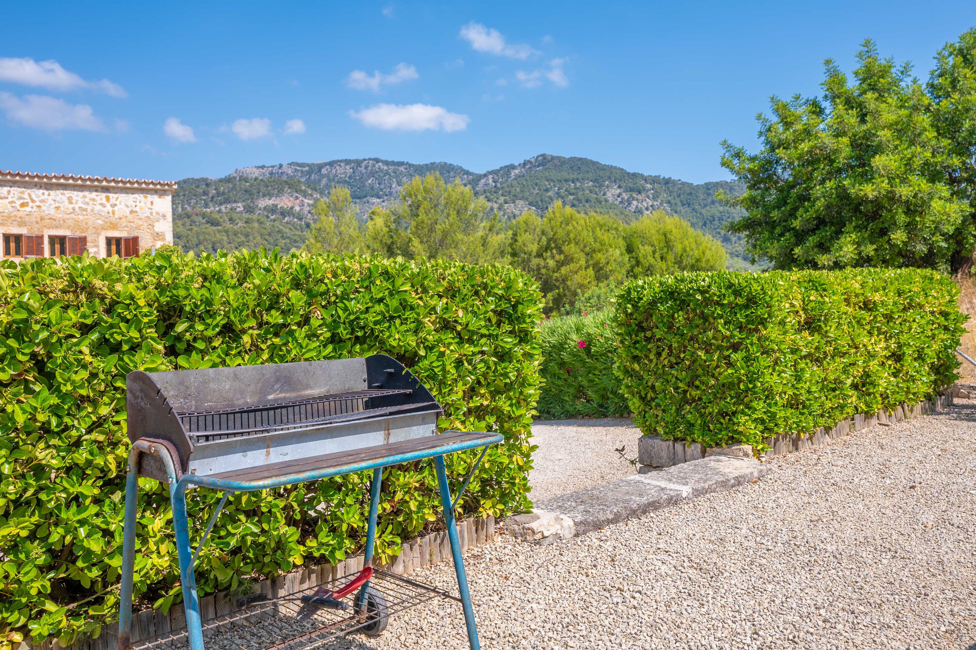A barbecue grill on a stand in a garden with a view of mountains and a building in the background.