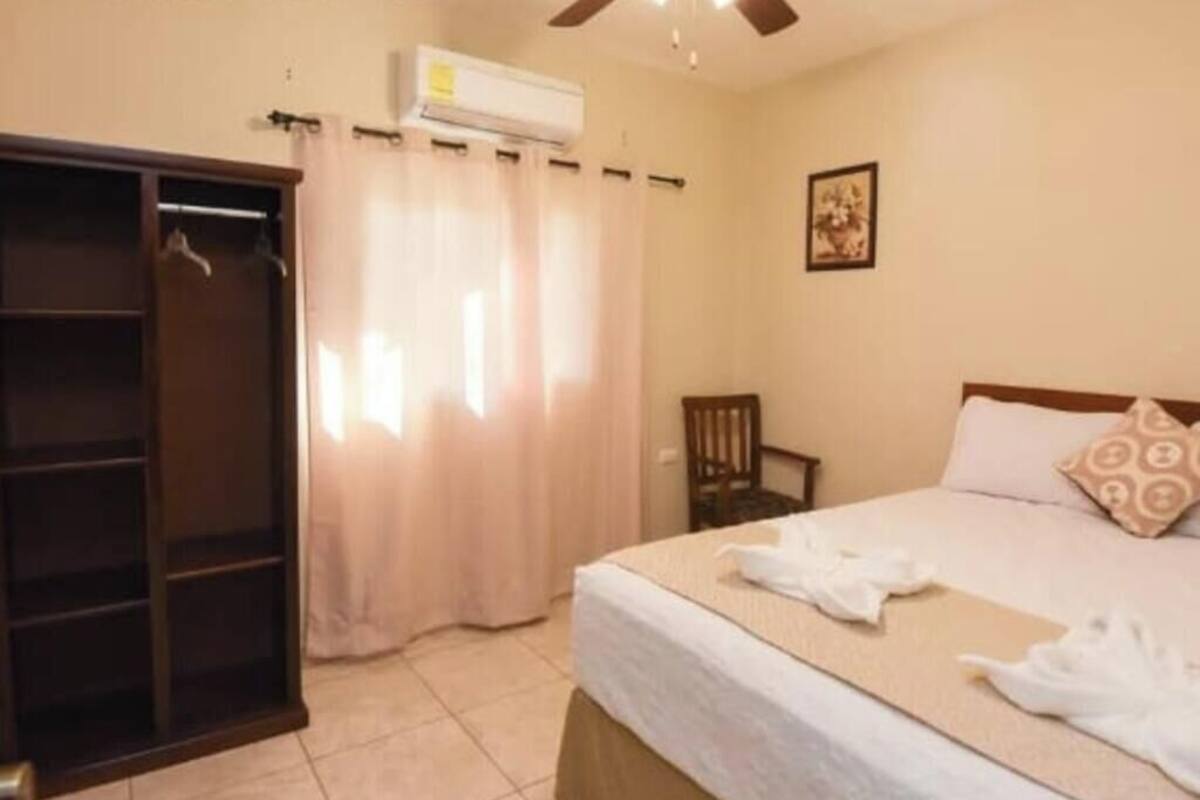 Una habitación de hotel con una cama, un armario, una silla y un equipo de aire acondicionado.