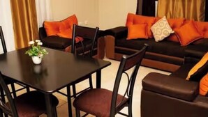 A dining area with a table and chairs, a sofa with orange cushions, and a small plant on the table. - Ecoturismo Monte Horeb (Gracias)