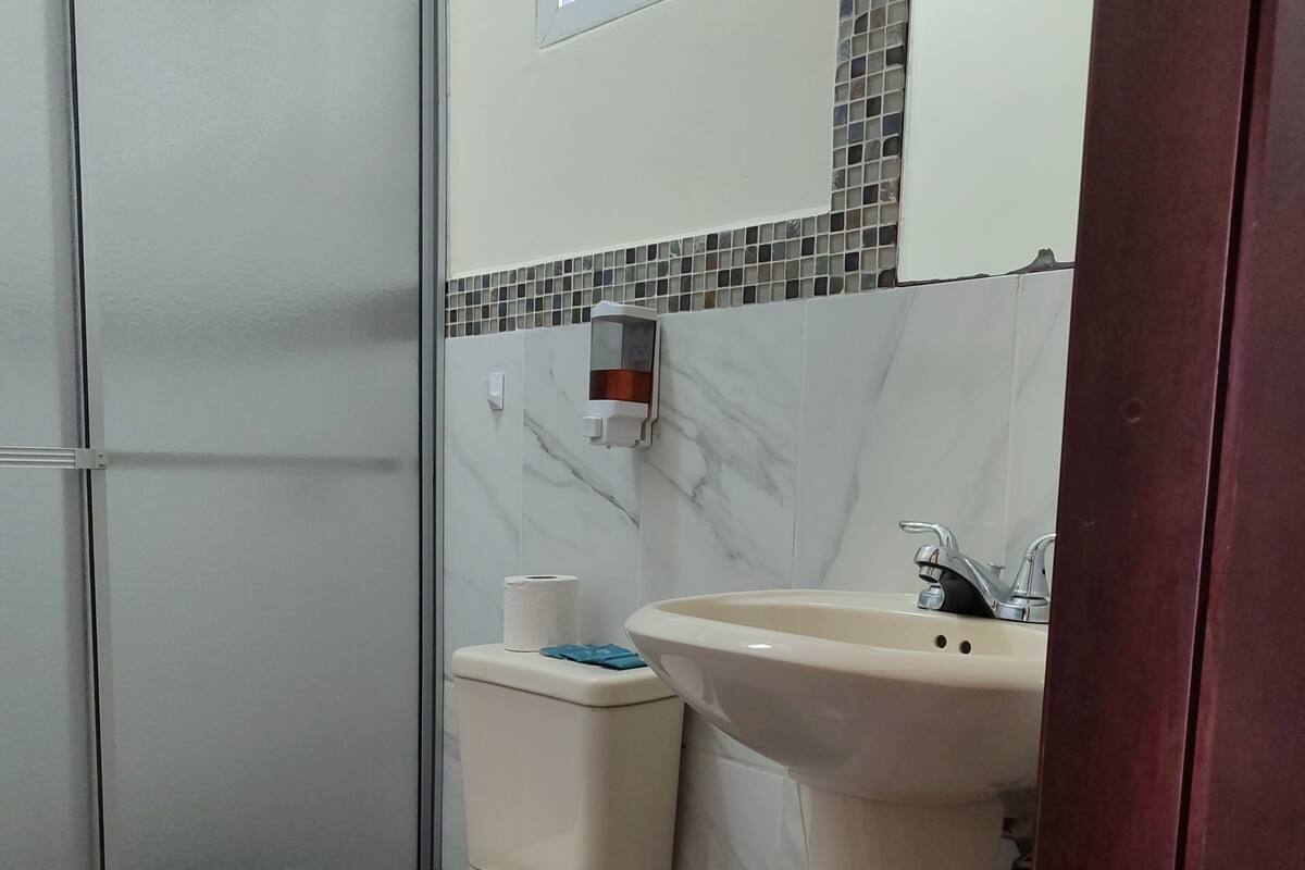 Un baño con inodoro, lavamanos, ducha y una ventana pequeña.