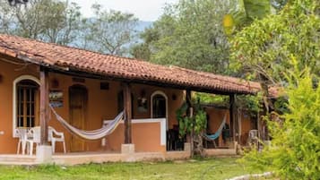 Una casa con techo de tejas, un porche con sillas y una hamaca.