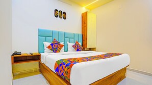 Een moderne slaapkamer met een houten bedframe, een blauw hoofdeinde en kleurrijke geometrische kussens.