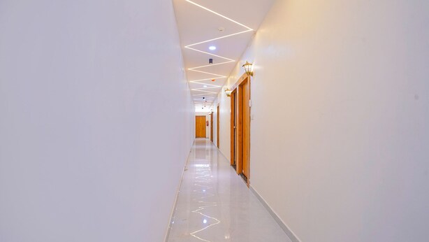 Een moderne, goed verlichte gang met een glanzende vloer, houten deuren en geometrisch vormgegeven plafondverlichting.
