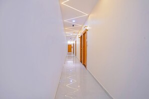Un couloir moderne et bien éclairé, doté d’un sol brillant, de portes en bois et d’un éclairage au plafond aux motifs géométriques.