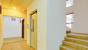 A hallway with a fire extinguisher, a door, and a staircase with wooden steps. - Fabhotel The Walnut (Pune)